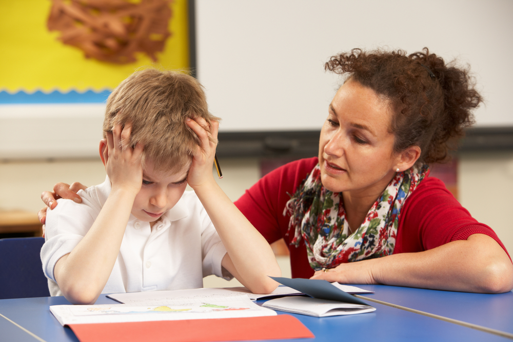 White stressed primary schoolboy with mixed race female teacher